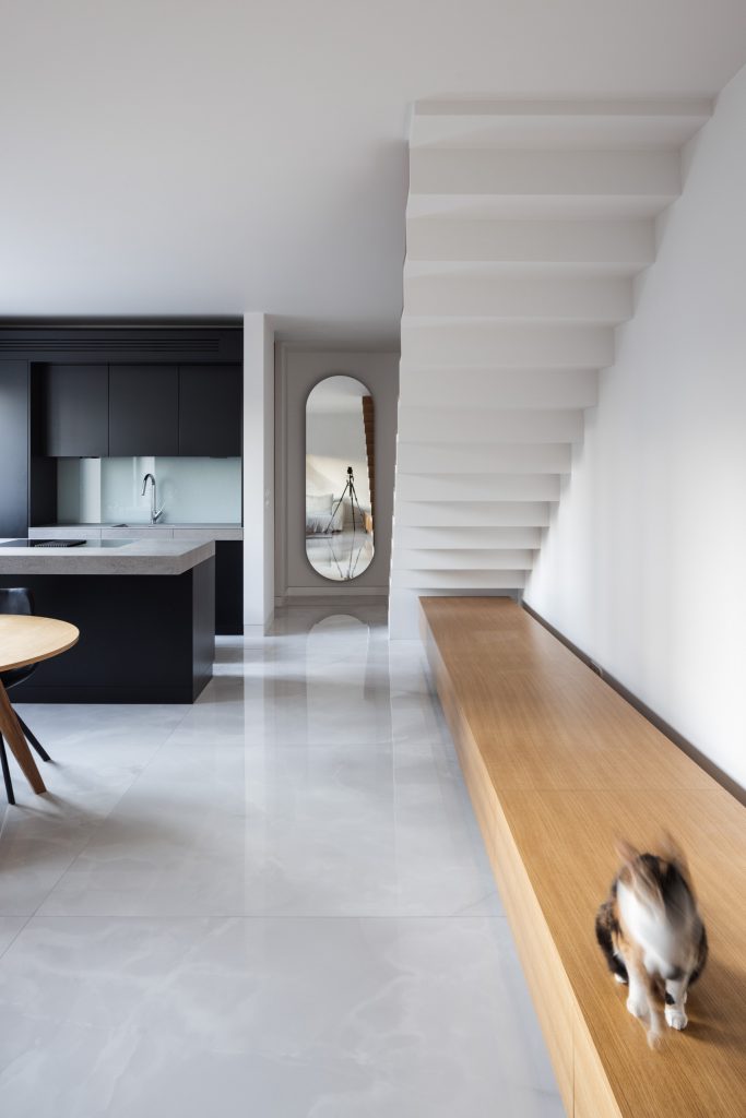 Moderná svetlá obývačka so schodiskom a čiernou kuchyňou