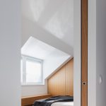 Biela podkrovná spálňa s drevenými skosenými dverami