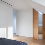Biela podkrovná spálňa s drevenými skosenými dverami