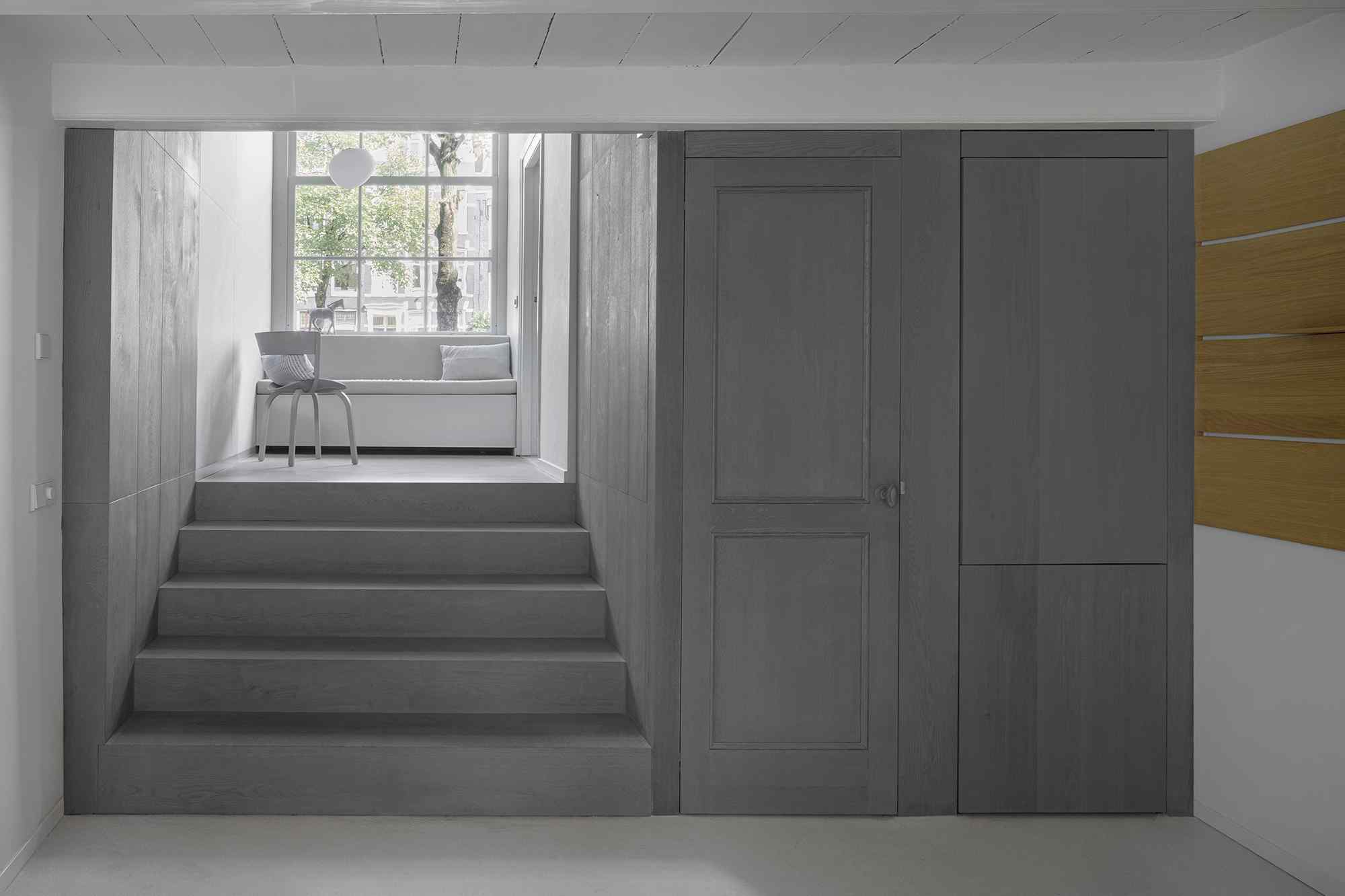 Sivé vzostupné schodisko k posedeniu pri okne v úzkom dome