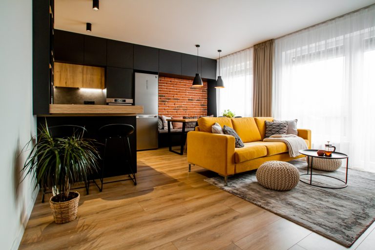 Obývačka so žltým gaučom čiernohnedou kuchyňou v industriálnom štýle