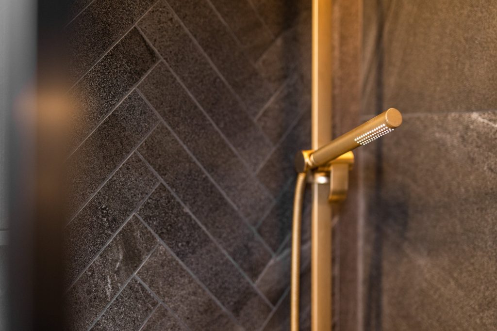 Mosadzná sprcha v tmavohnedej kúpeľni