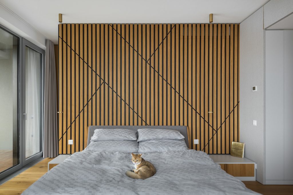 Sivá posteľ s mačkou pred čiernohnedou lamelovou stenou