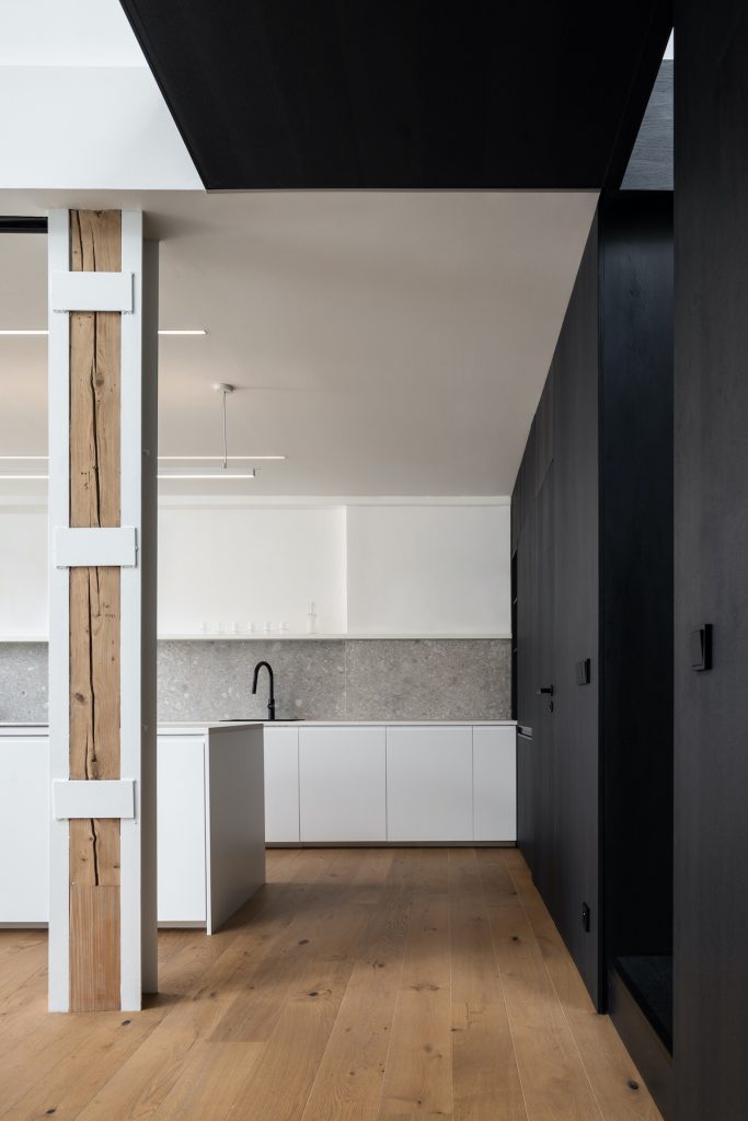 Biela kuchyňa s čiernym boxom a drevenou podlahou