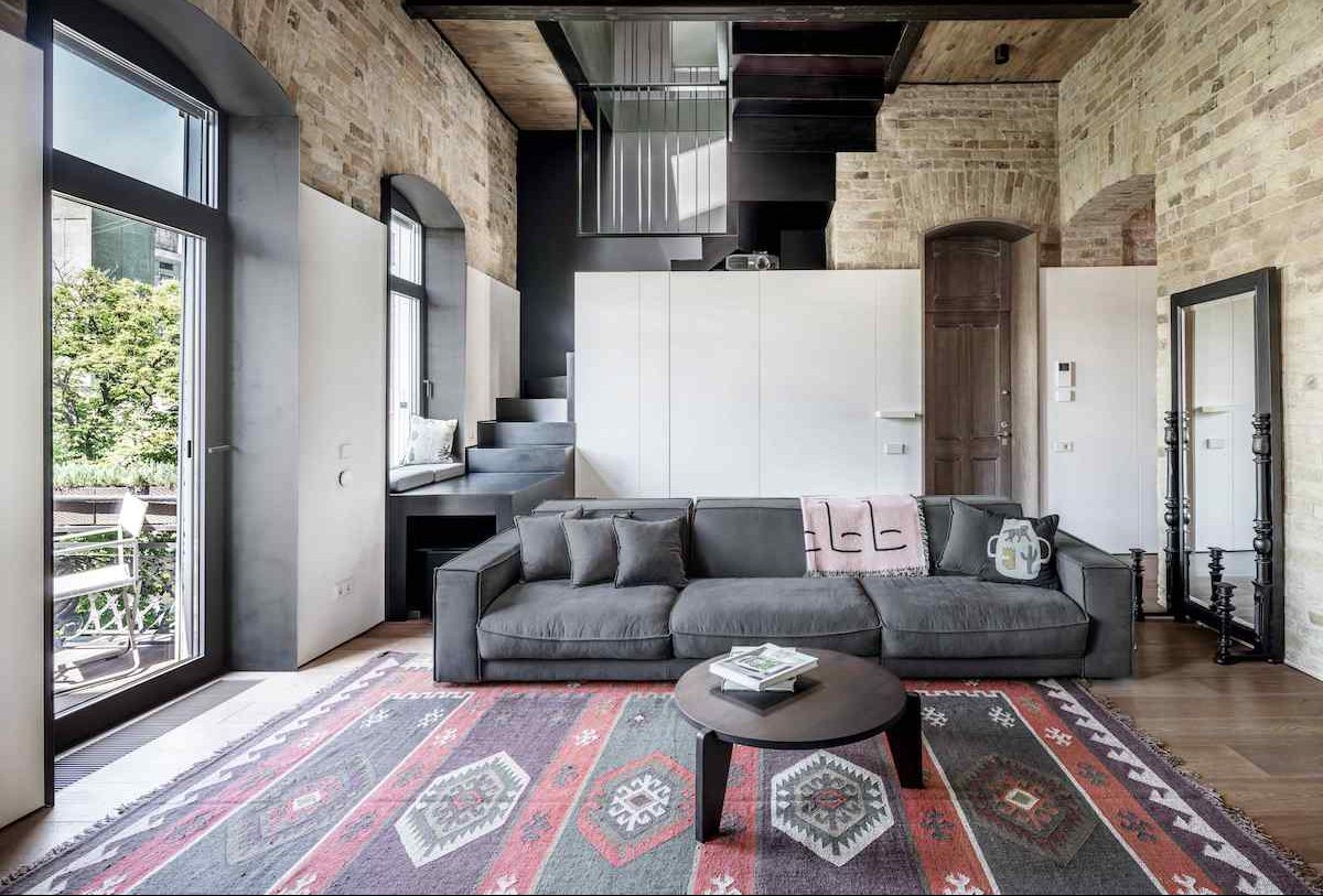 Podkrovie je realizované ako moderný loft bez historických prvkov, ale vďaka rovnakej monochromatickej palete pôsobí ako prirodzené rozšírenie prízemia.