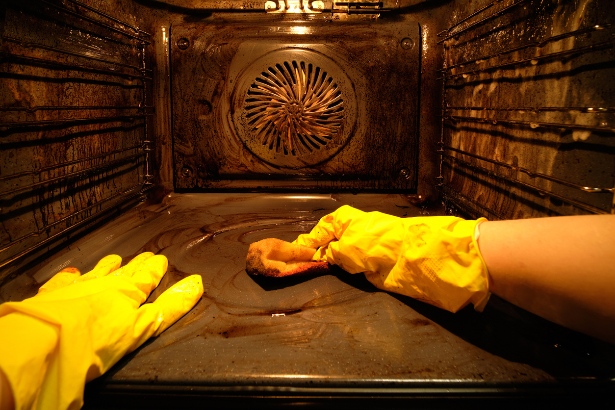 A person in protective gloves washes the dirty oven from traces of food inside with the light on