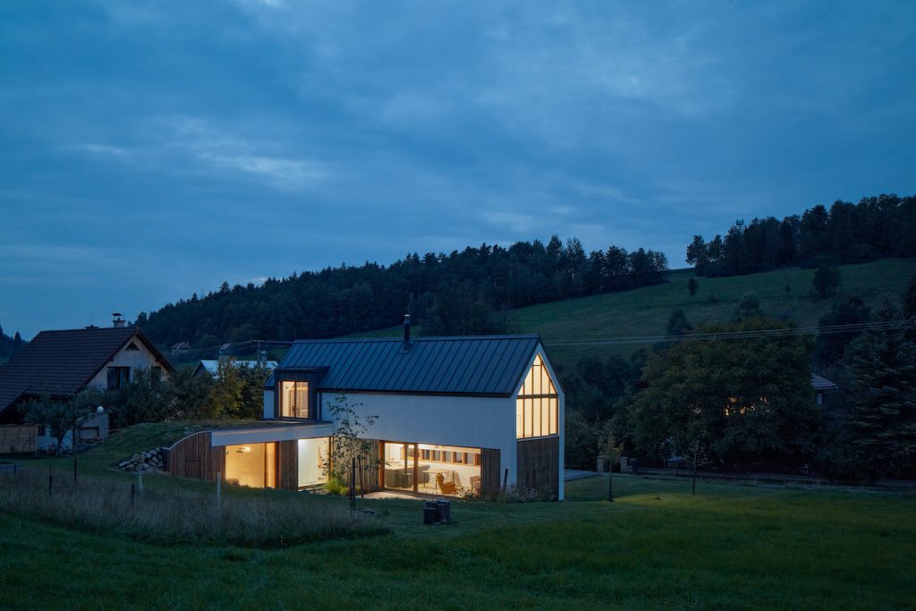Moderný bielodrevený rodinný dom so šikmou strechou a presklením na lúke