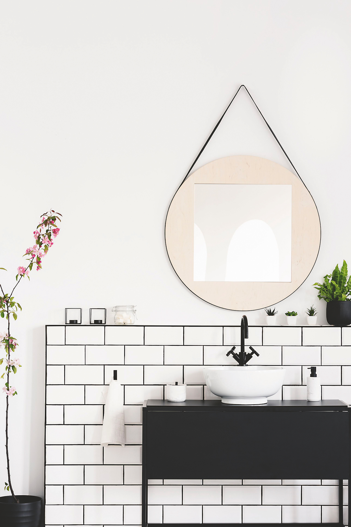 Real photo of a black cupboard, round mirror and white tiles in a modern bathroom interior