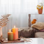 Burning candles with autumn decor on white table at home