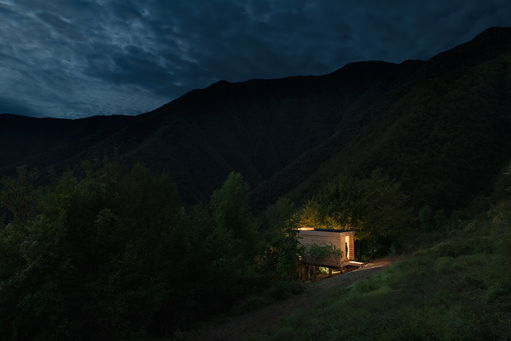 Exteriér osvetleného príbytku v noci - Drevená pustovňa Hermitage Cabin v Taliansku