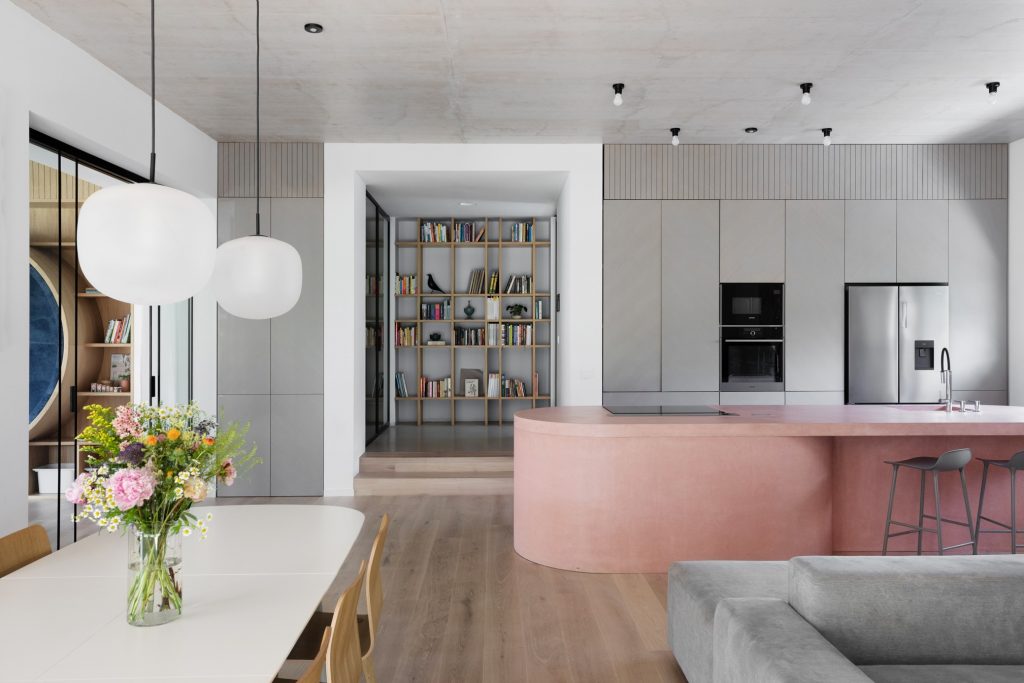 obývačka a kuchyňa s ružovým kuchynským ostrovom a betónovým stropom