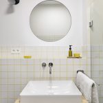 kúpeľňa s bielym obkladom a žltou škárovačkou, umývadlo s okrúhlym zrkadlom