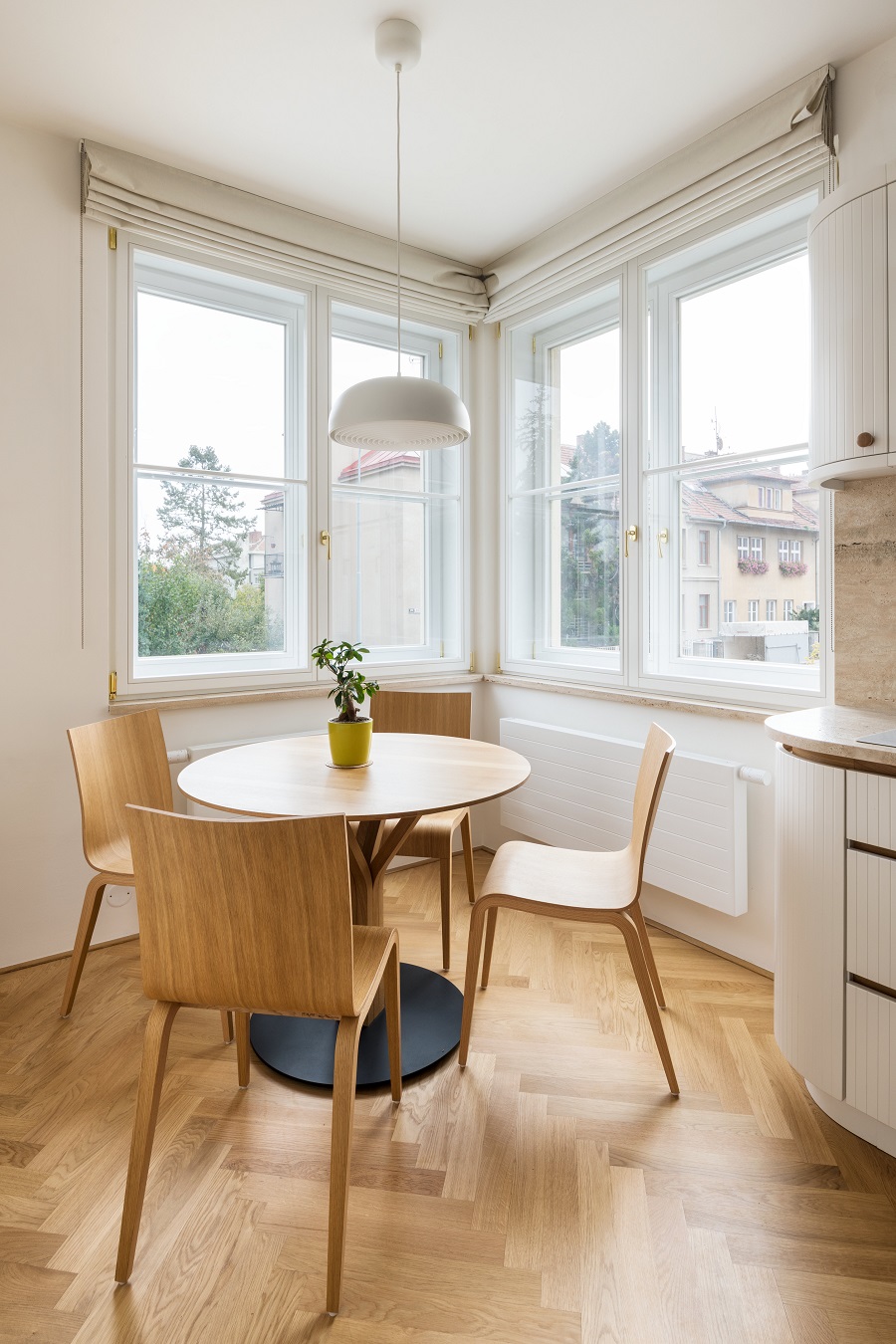 okrúhly jedálenský stôl z bledého dreva a štyri stoličky v kuchyni s rohovým oknom