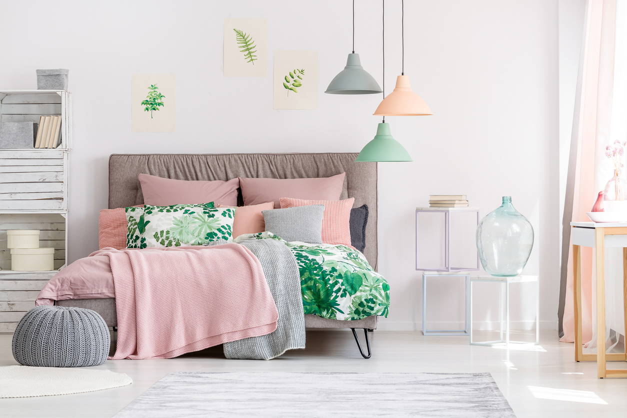 spálňa s doplnkami v pastelových farbách, posteľ, ružová deka, zelená deka, vankúš so vzorom, lampa