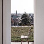 výhľad cez otvorené dvere na krajinu s kostolom, vintage stolička
