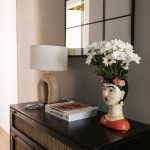 Porcelánová váza v tvare ázijskej ženy s bielymi kvetmi na vintage komode s retro stolovou lampou