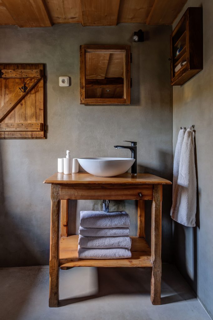 Kúpeľňa s okrúhlym keramickým umývadlom na dradičnom drevenom stolíku v chalupe