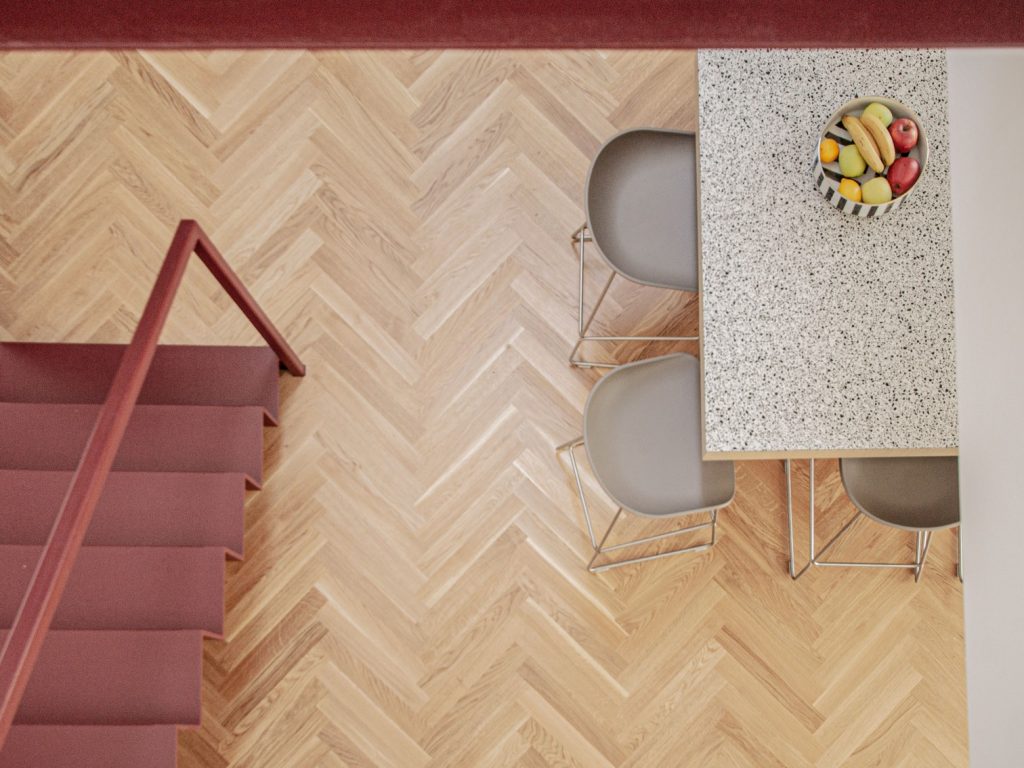 pohľad zvrchu na parketovú podlahu, červené schodisko a kuchynský ostrov s dvomi stoličkami