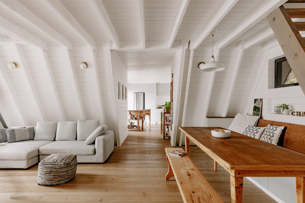 interiér chaty s lomeným bielym trámovým stropom, sivou sedačkou a stolom zo svetlého dreva