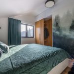 spálňa s tapetou s motívom lesa a zelenou prikrývkou na posteli