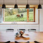 výhľad z kuchyne cez okno na lúku, kde sa pasú dva kone, ponad drevený jedálenský stôl