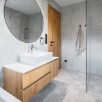 kúpeľna so sivými obkladačkami, umývadlom na skrinke a okrúhlym zrkadlom, sprchovací kút