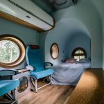 interiér inšpirovaný lietadlom, modré steny, okrúhle okná, posteľ, kreslá ako z lietadla