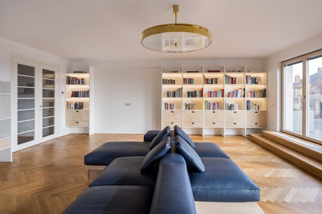 veľká obývačka s tmavomodrou sedačkou, bielou knižnicou a drevenou podlahou