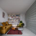 obývačka s knižnicou a žltou sedačkou a sklobetónovou stenou