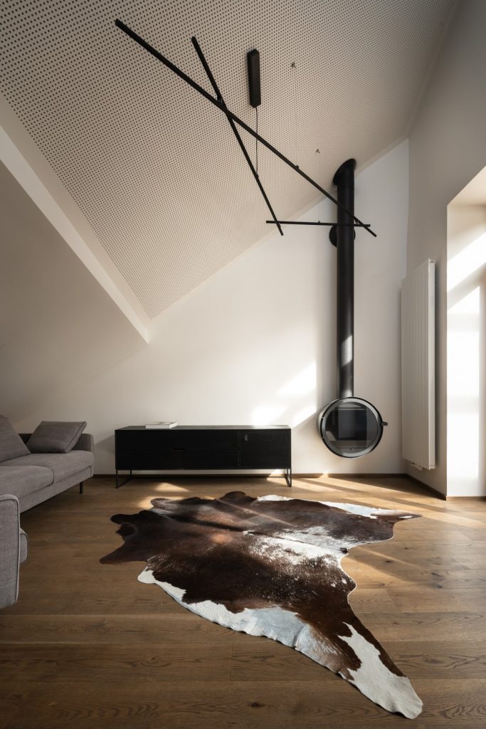 obývačka s oceľovým krbom, sivou sedačkou a kravskou kožou na podlahe