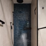 Sprchovací kút s modrým obkladom na zadnej stene a čiernou sprchou