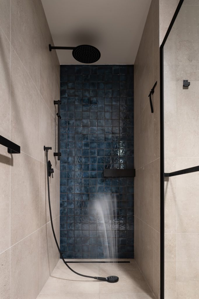 Sprchovací kút s modrým obkladom na zadnej stene a čiernou sprchou