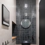 kúpeľňa s pásom sivého obkladu, umývadlom a okrúhlym zrkadlo