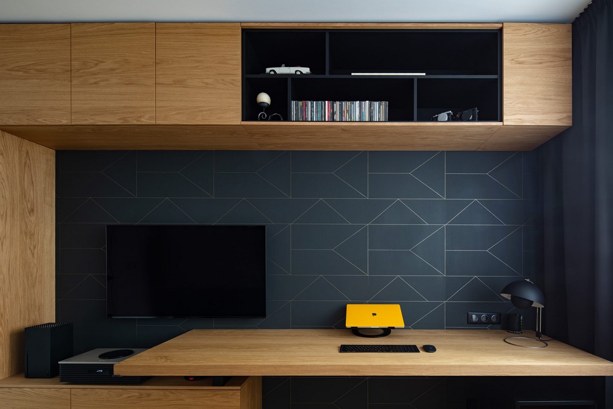 pracovňa s monitorom, dreveným nábytkom a geometrickým vzorom na modrej stene