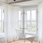 biela vypletaná stolička oproti bielym oknám, drevená podlaha