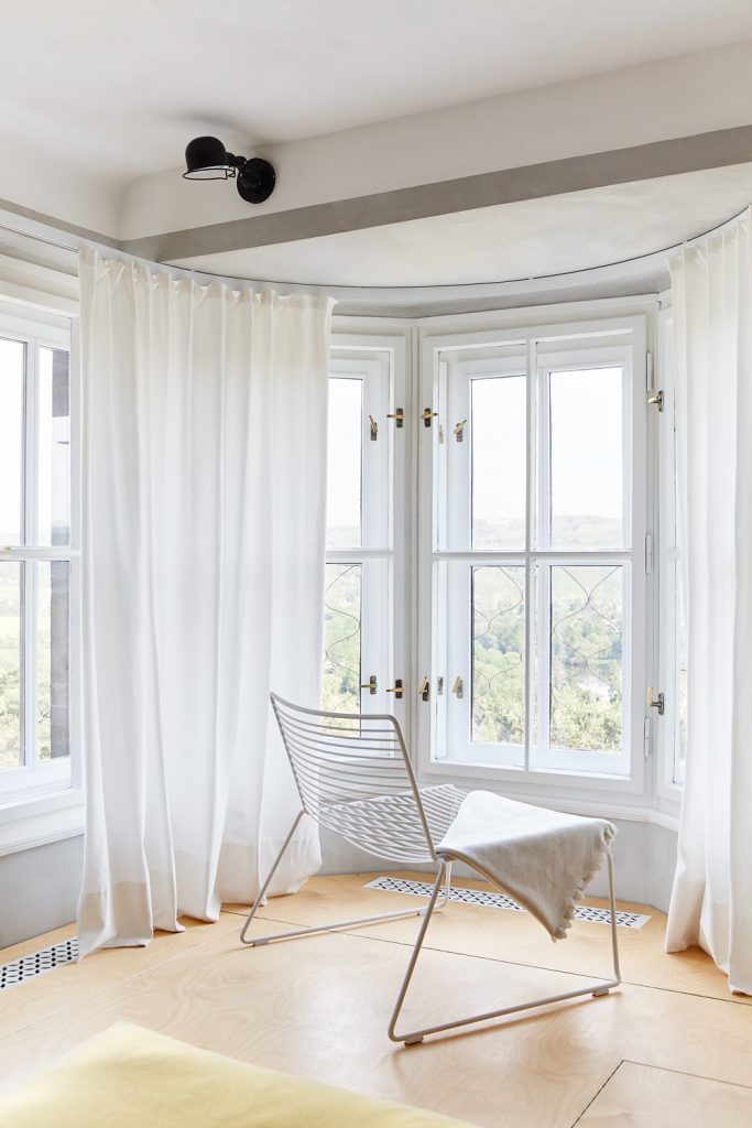 biela vypletaná stolička oproti bielym oknám, drevená podlaha