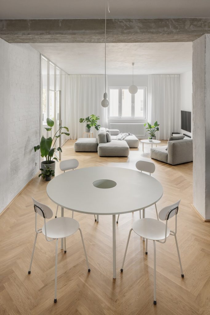 otvorený denný priestor s jedálenským stolom, sivou sedačkou a dubovou podlahou