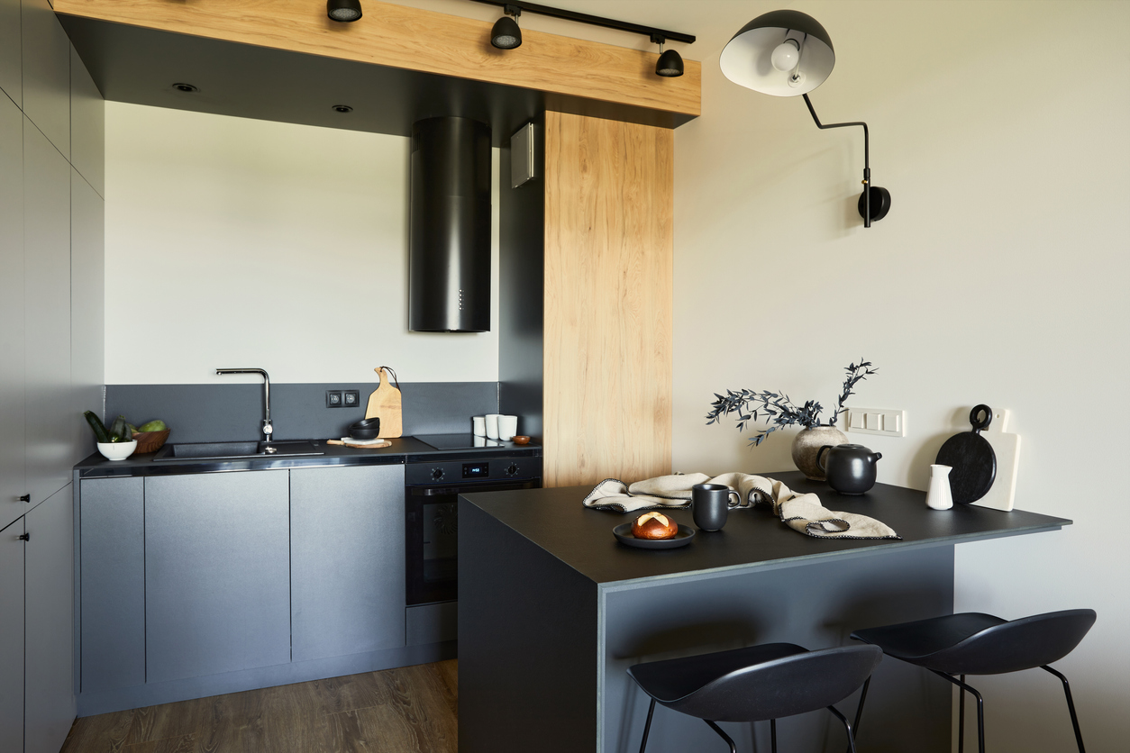 Stylish composition of modern kitchen and dining room interior in small apartment. Black furniture, kitchen island and wooden kitchen accessories. Creative wall. Template.