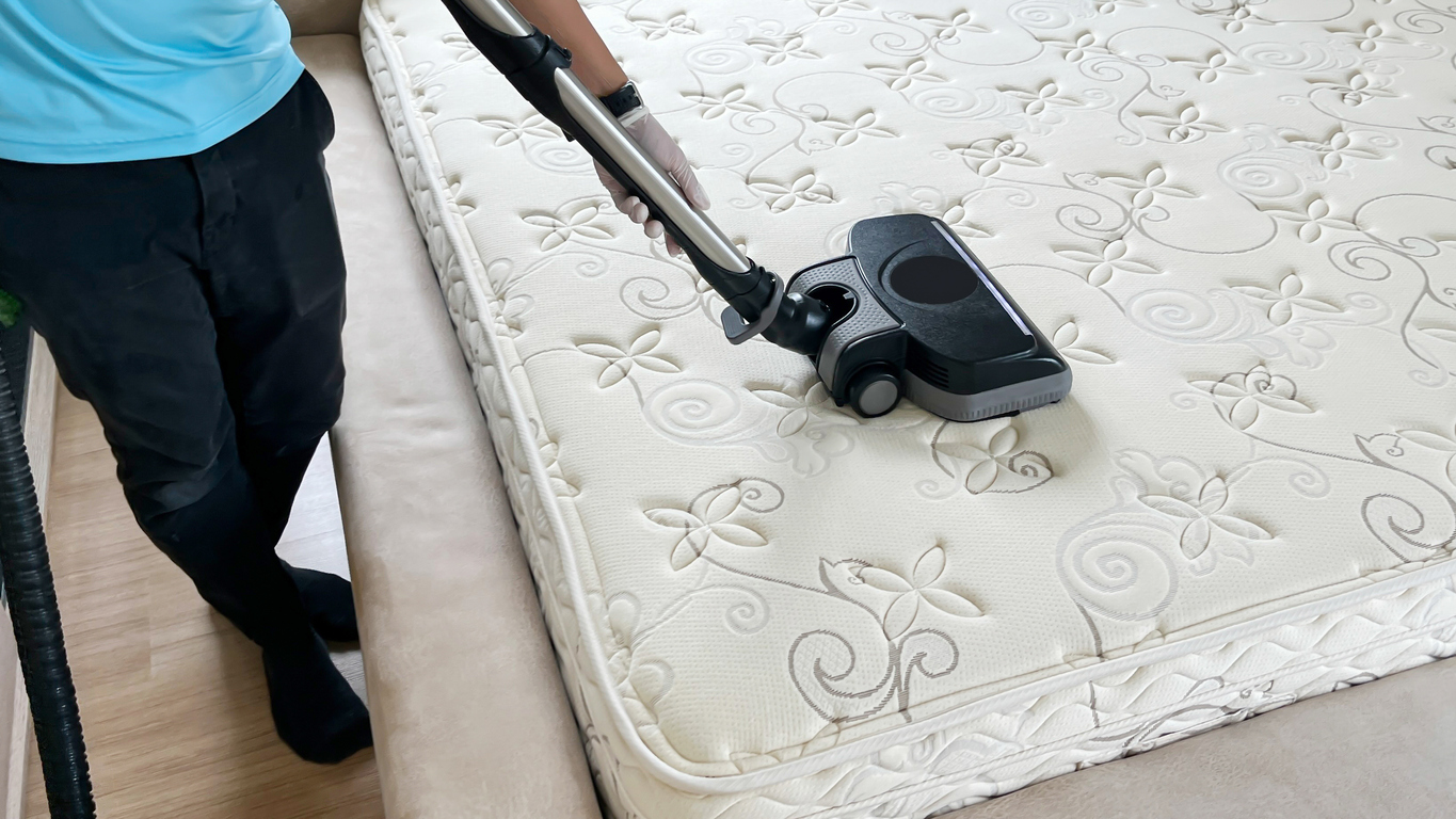 Professional cleaning and sanitizing services use industrial vacuum cleaner to clean and get rid of dust mites from a mattress in the bedroom.