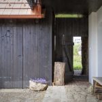 Pohľad do zrekonštruovanej stodoly s čiernou drevenou fasádou cez otvorené dvere