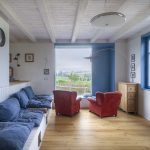denný priestor s bielym palubovkovým stropom, červenými kreslami a modrými rámami okien na chalupe