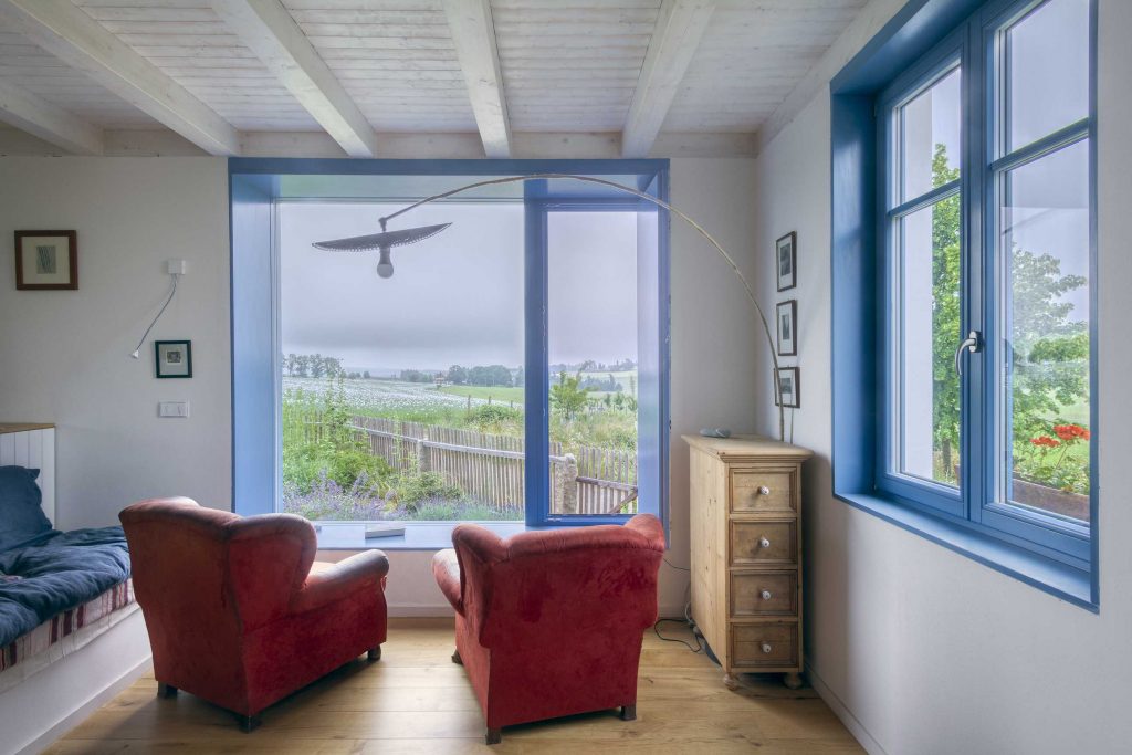 denný priestor s bielym palubovkovým stropom, červenými kreslami a modrými rámami okien na chalupe