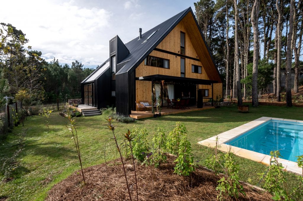 dom obložený svetlým drevom s čiernou štítovou strechou, bazén
