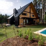 dom obložený svetlým drevom s čiernou štítovou strechou, bazén