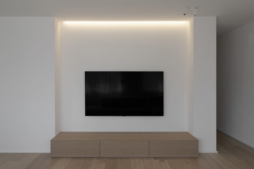 televízor na bielej stene, pod TV drevená skrinka