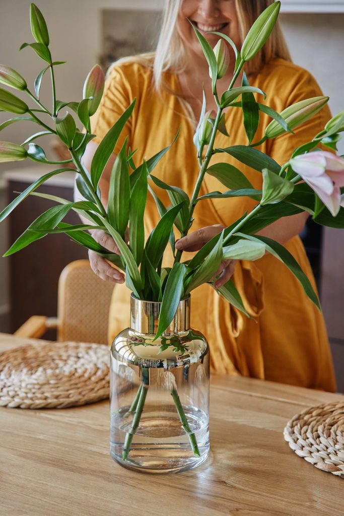 0detail na sklenenú vázu s kvetmi, v pozadí žena v žltých šatách