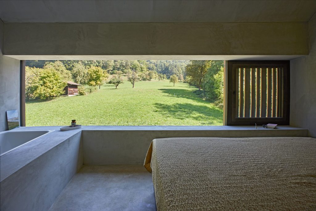 spálňa, steny s betónovým vzhľadom, výhľad cez okno do prírody
