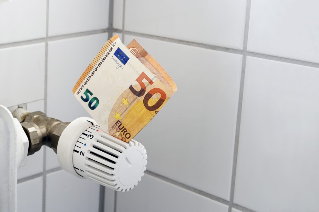 Euro banknote stuck in the thermostat of an heating radiator, rising costs for heat and energy, home finance and money concept, copy space, selected focus