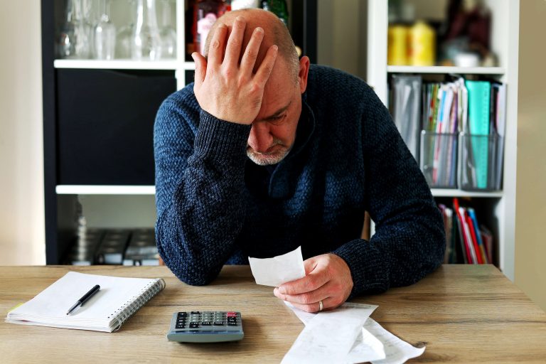 nešťastný starší muž sa díva na kus papiera, kalkulačka