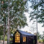 Malý dom na lesnej čistinke s čiernym opláštením